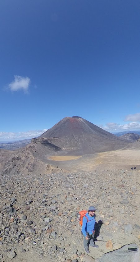Hiker on barren, rocky landscape, with volcano in background