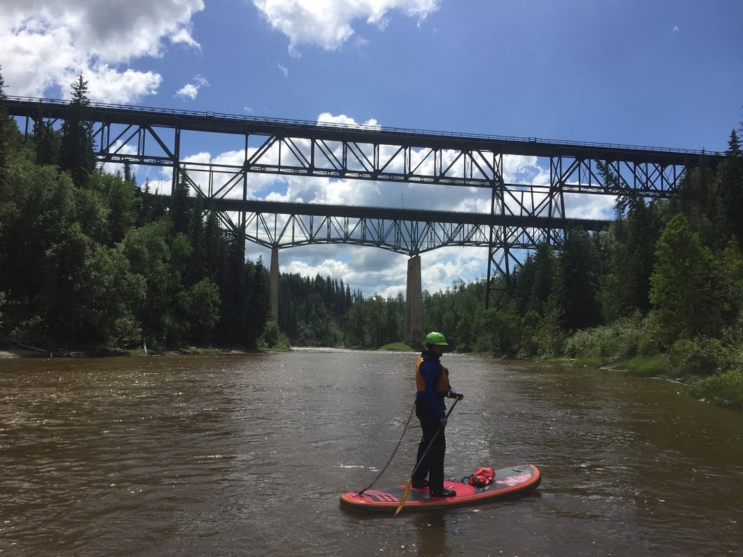 SUP paddler on river in front of two trestle bridges