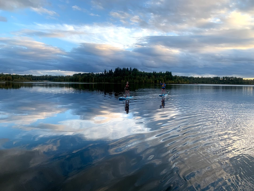Two paddle boarders on glassy lake reflecting the sky above